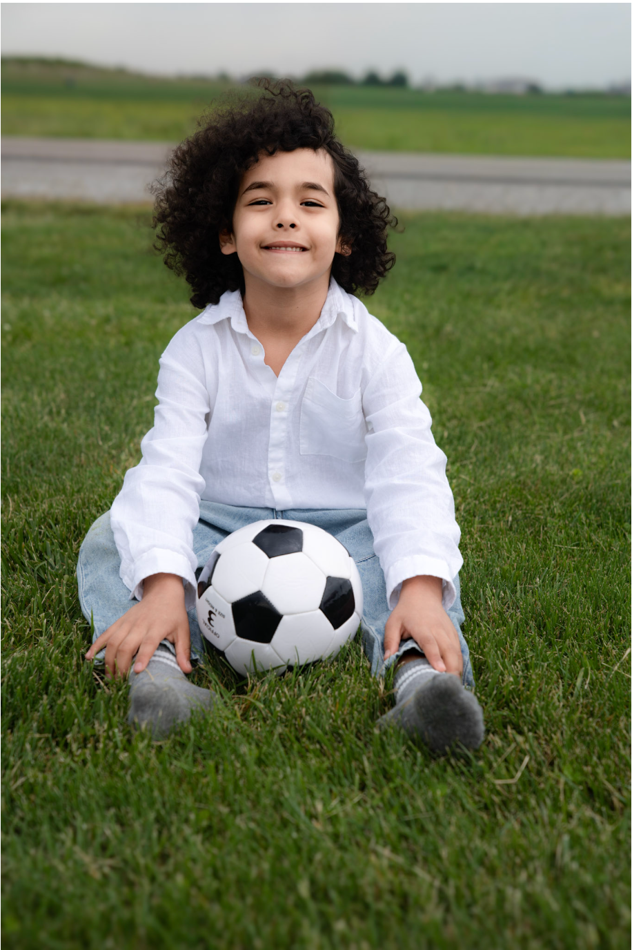 Child smiling outdoors with a soccer ball